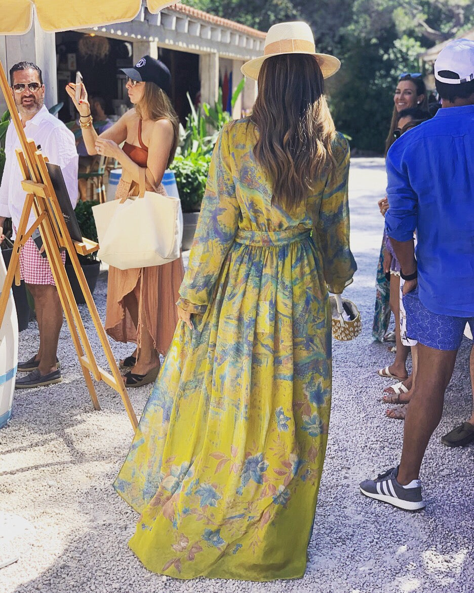 Woman in a yellow floral kimono dress walking outdoors with people around her.