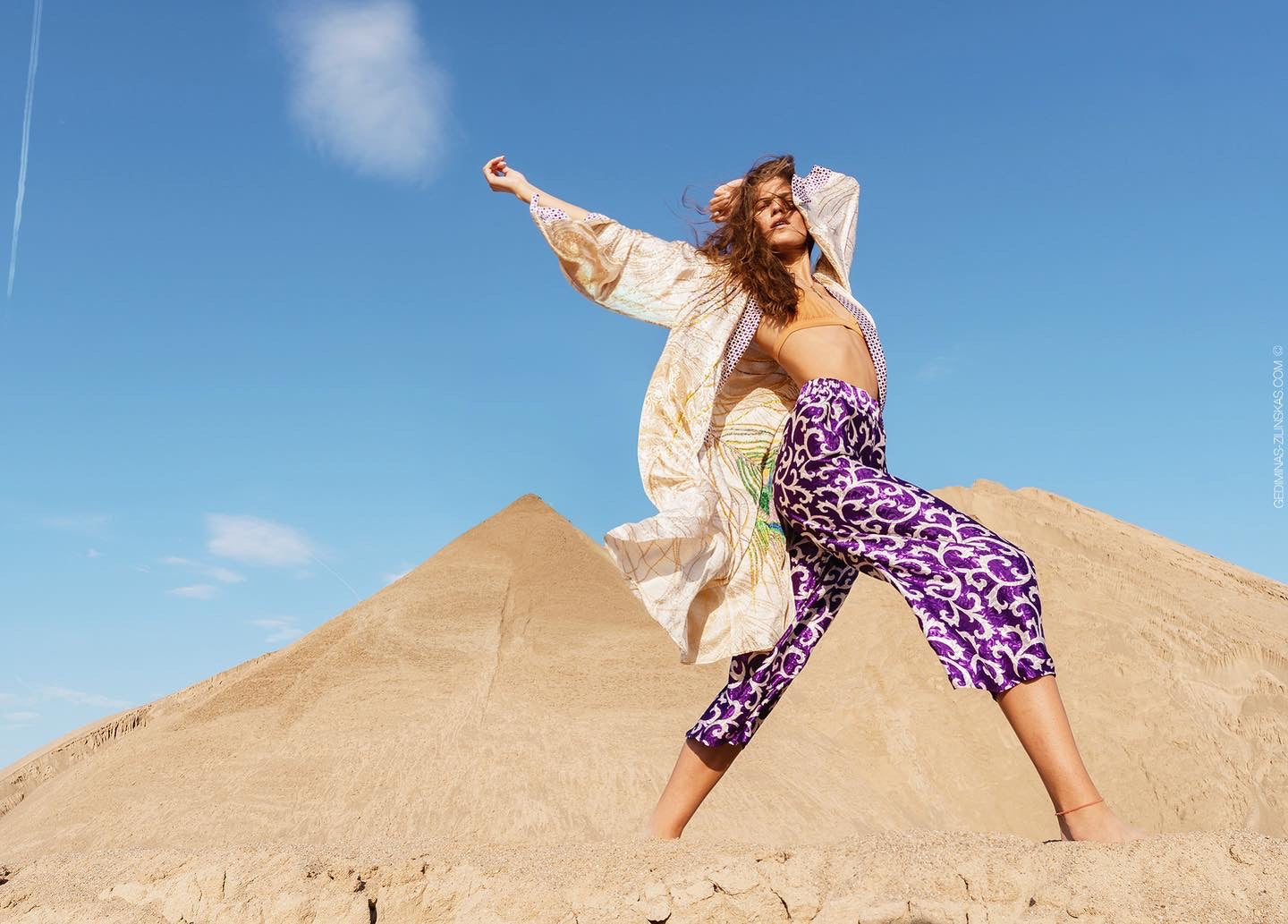 A woman in a desert setting wearing a beige golden kimono  and purple patterned silk pants.