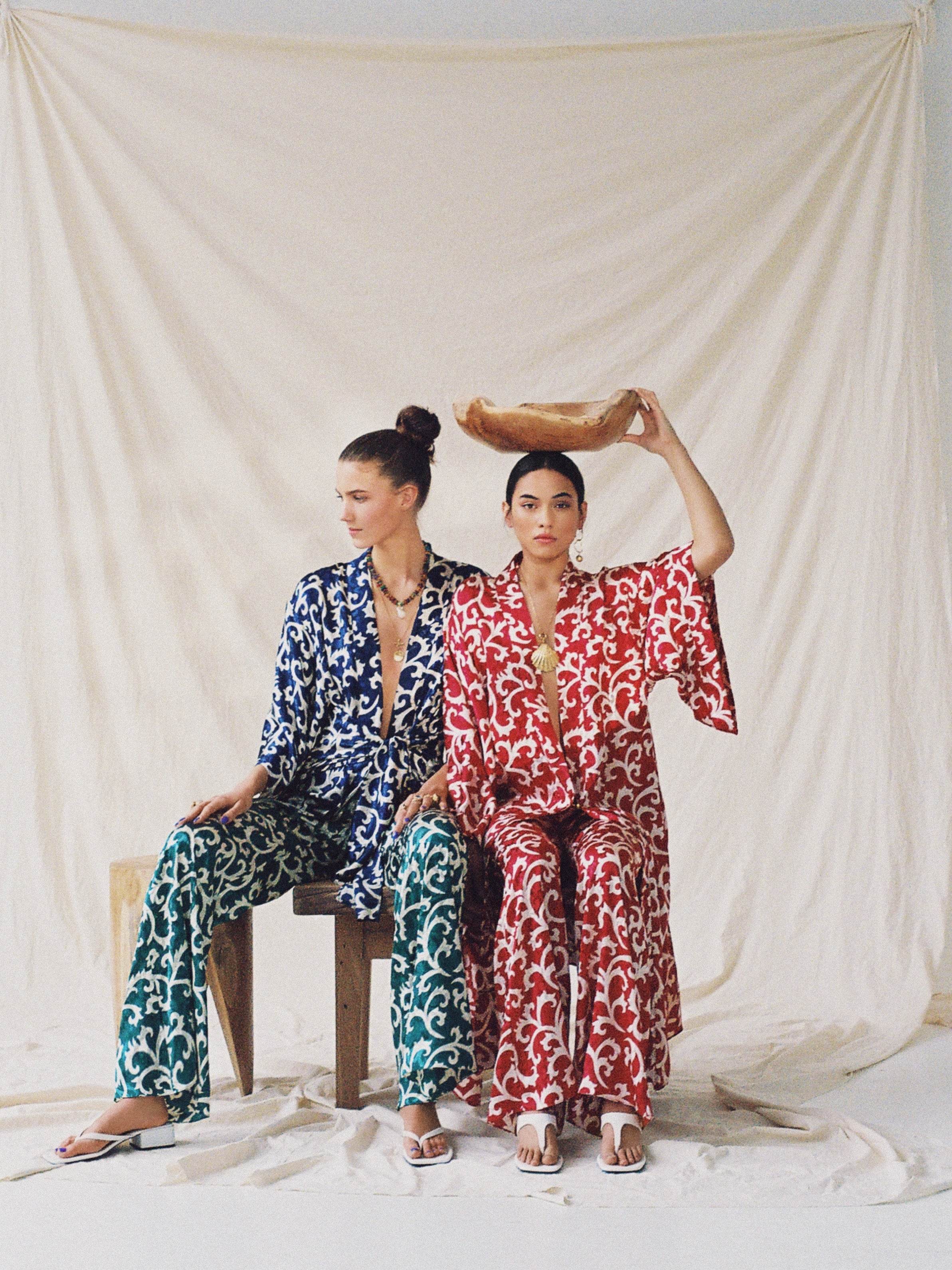 Two women in colorful Indian silk resort wear sitting against a plain background