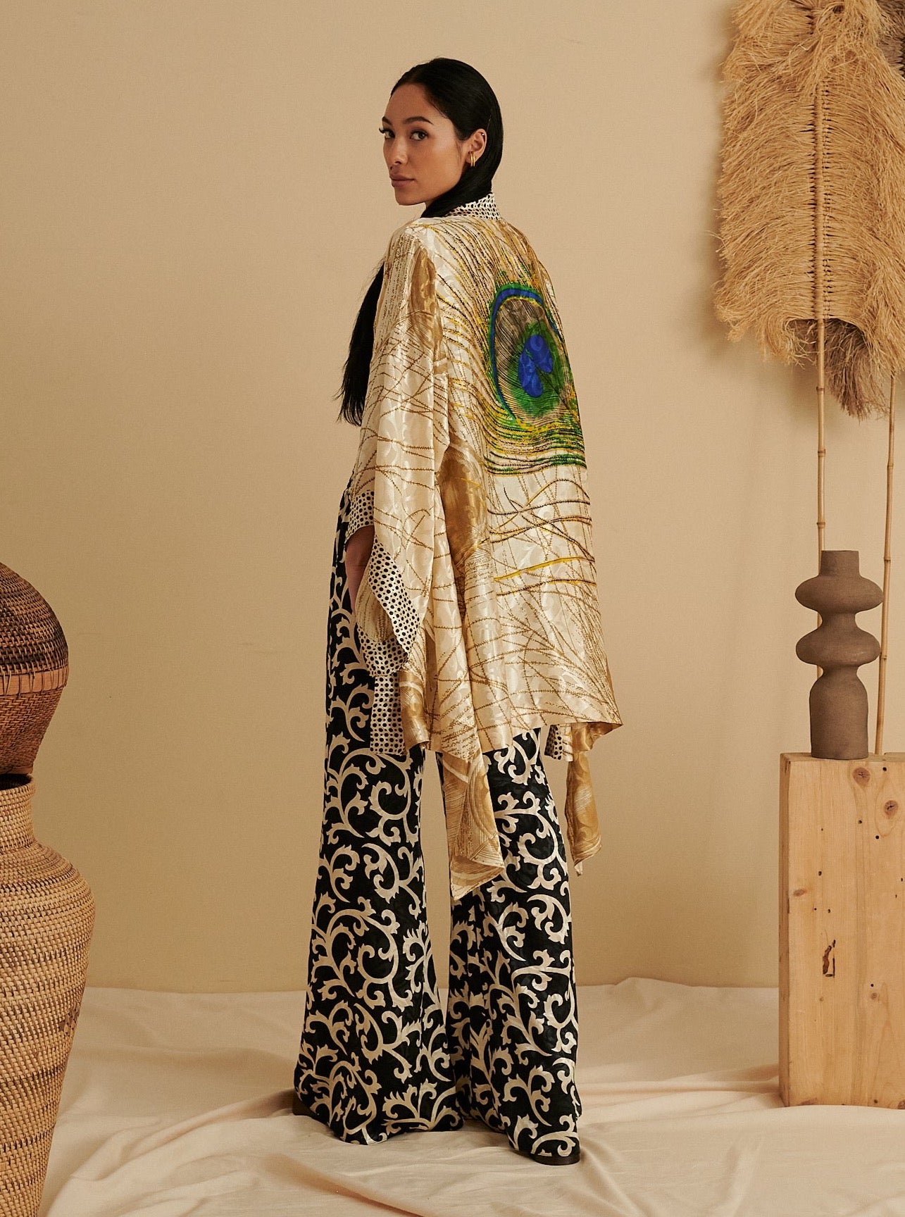 Sustainable handmade black and gold kimono with peacock feather design worn over organic patterned wide-leg pants in.