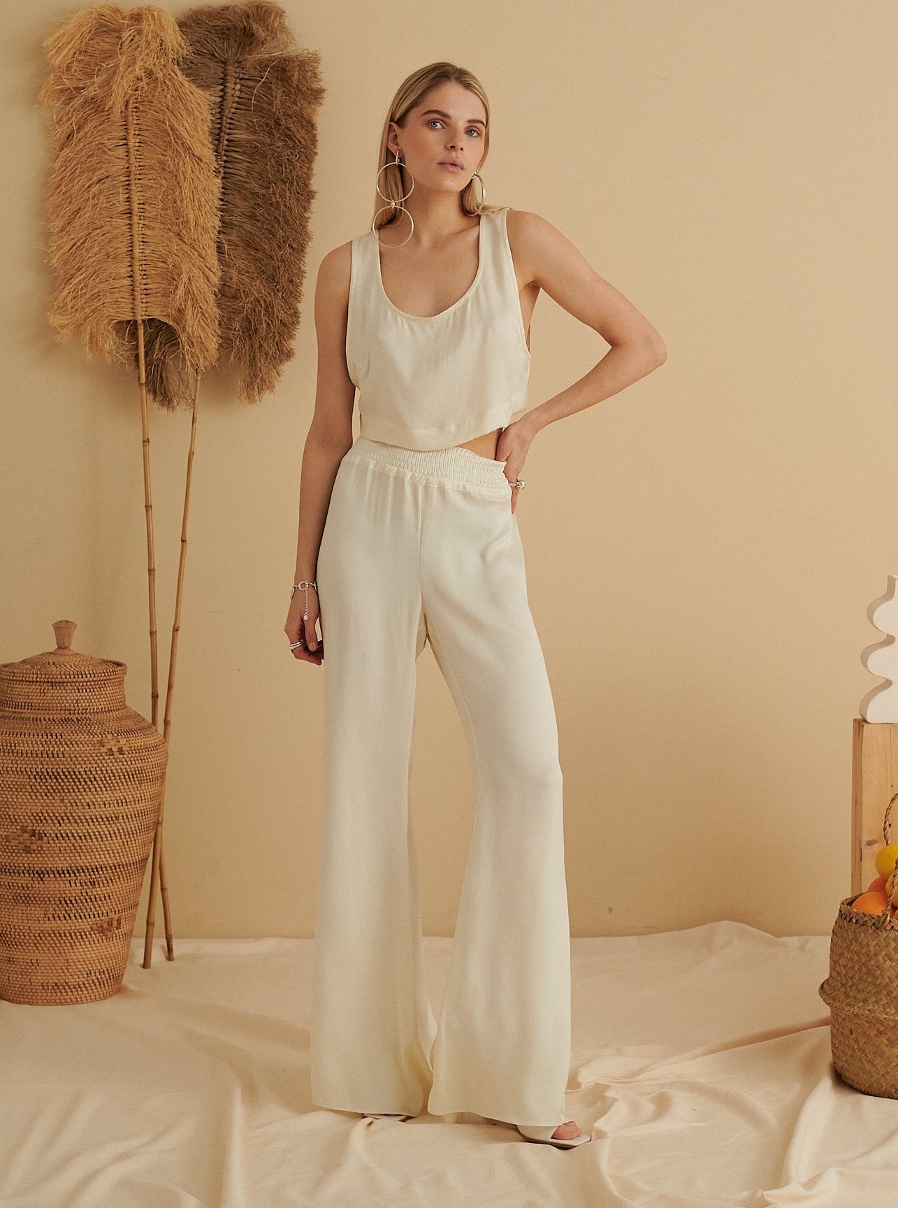 White dove flared trousers in eco-friendly cupro fabric, paired with a sleeveless cream organic top, styled in a minimalist.