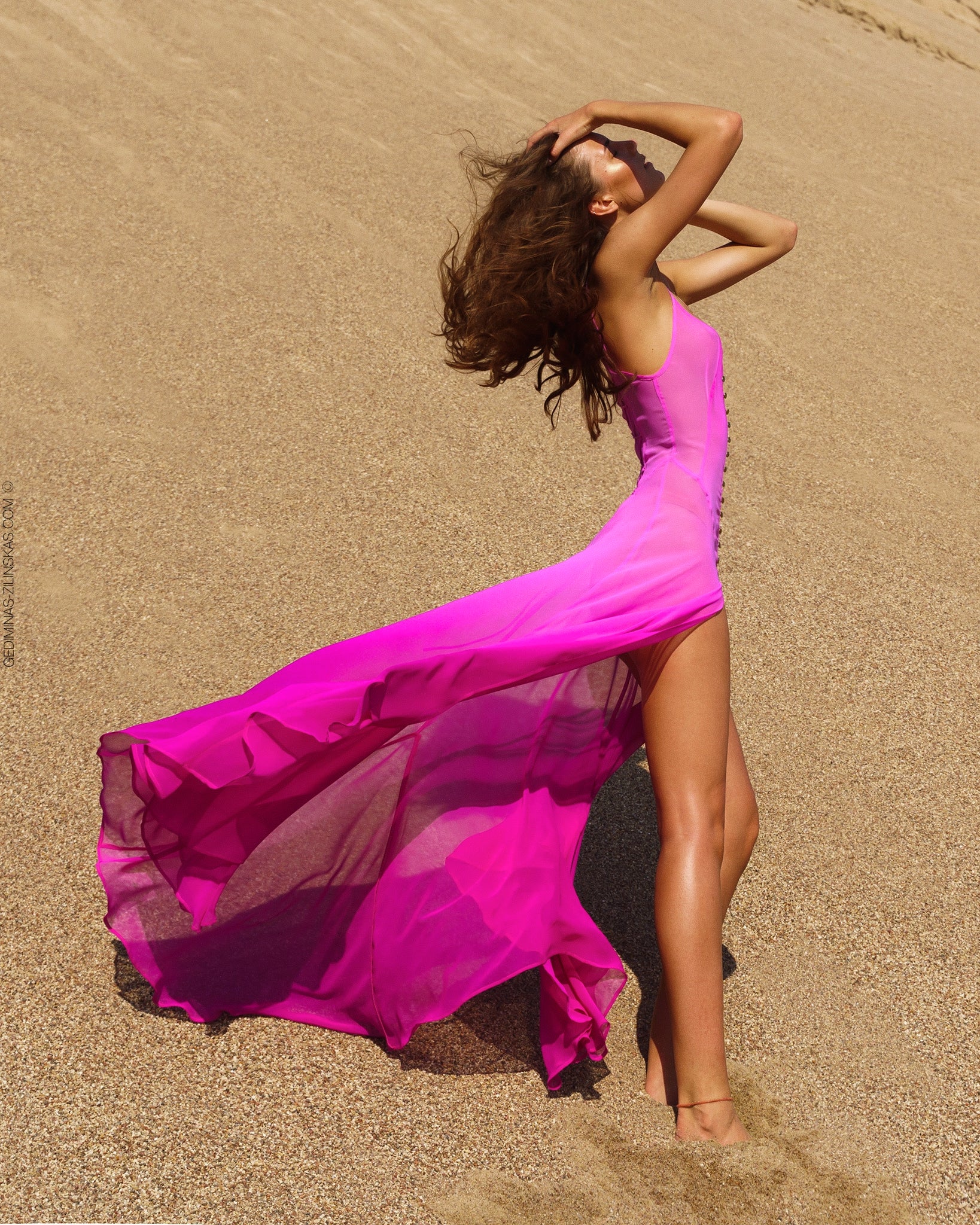 Woman in a flowing pink silk dress standing on sand