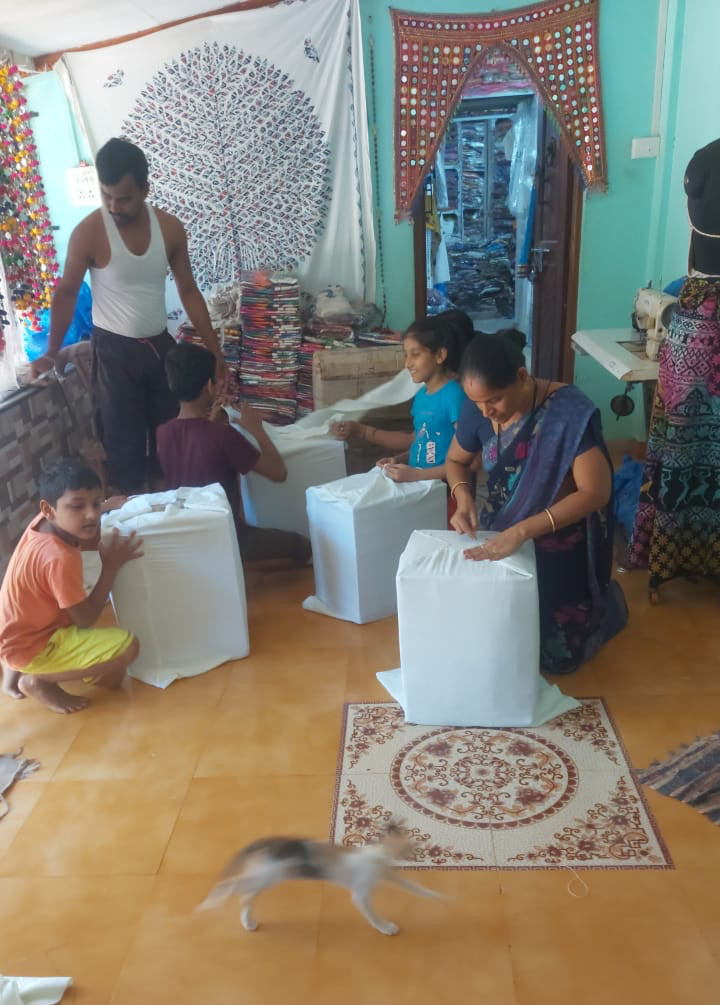 Indian family packing fabrics into white boxes in a room with colorful decorations.