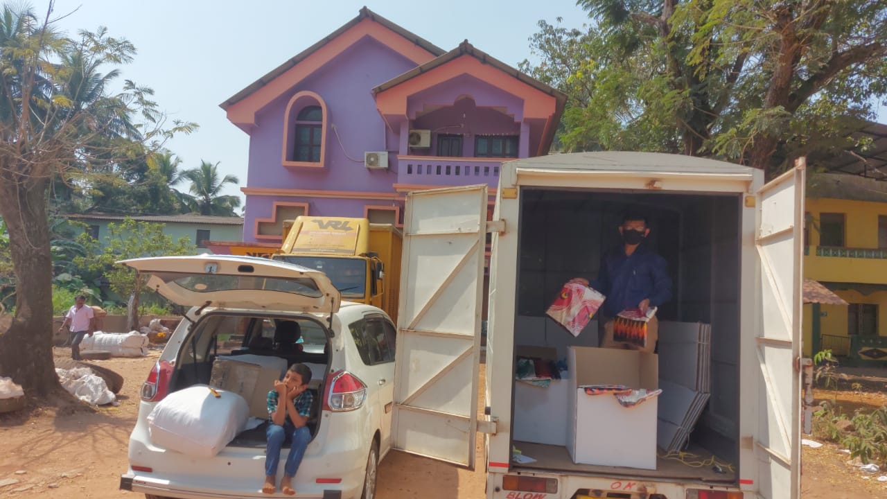 Van with open cargo area and people around a house with a purple roof.